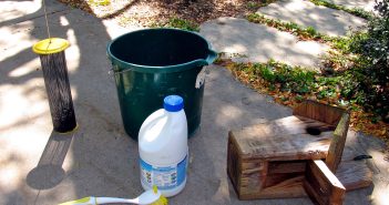 Image of green bucket, bottle of clorox, brush with handle and birdhouse with opened panel